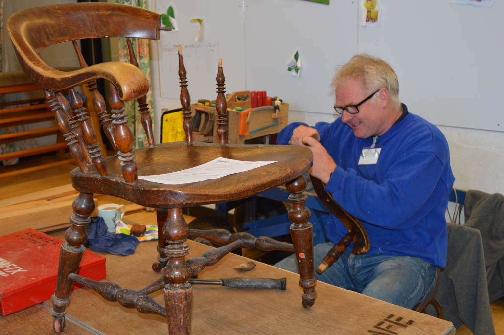 A man sits at a table fixing the arm of a chair