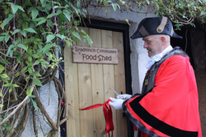Mayor in tradiational black hat and red coat cutting the ribbon on the food shed door