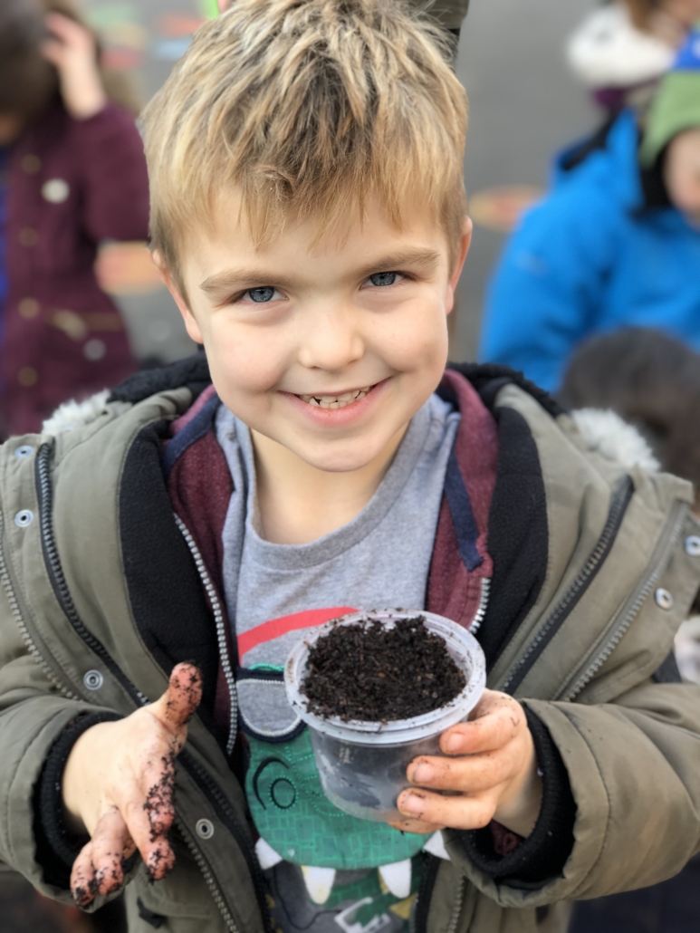 Child smiling and holding a pot of soil