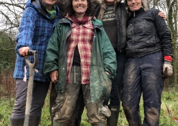 A small group of people wrapped up warm and muddy, one with a spade in her hand