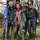 A small group of people wrapped up warm and muddy, one with a spade in her hand