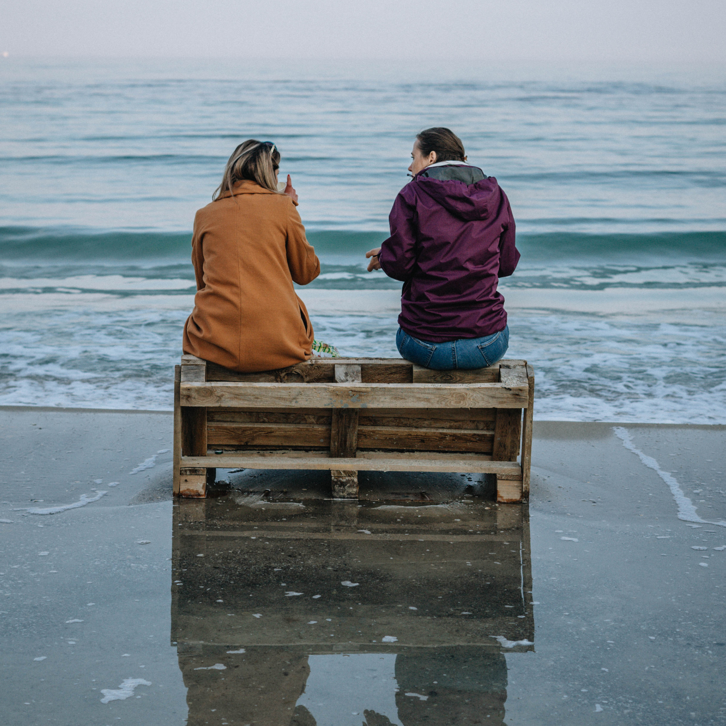 Two people sat facing the sea drinking coffee and talking